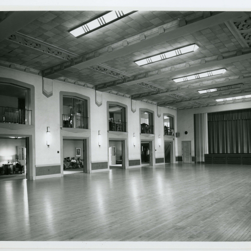 Empty room with wooden floor, archways and balconies, and stage at far end