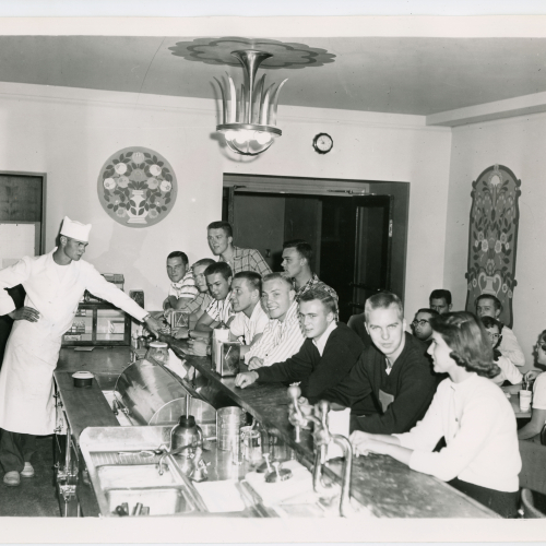 Customers seated at soda fountain counter and server in uniform