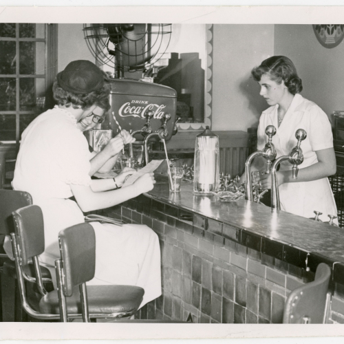Two women being served by third woman at soda fountain counter