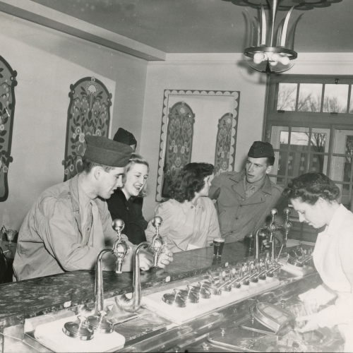 Two men in military uniform and two women being served by a woman at the soda fountain counter