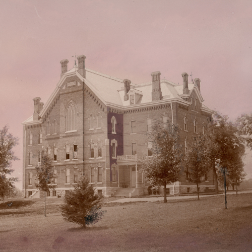 Three and a half story brick building with seven visible chimneys and pointed arched window on upper floor