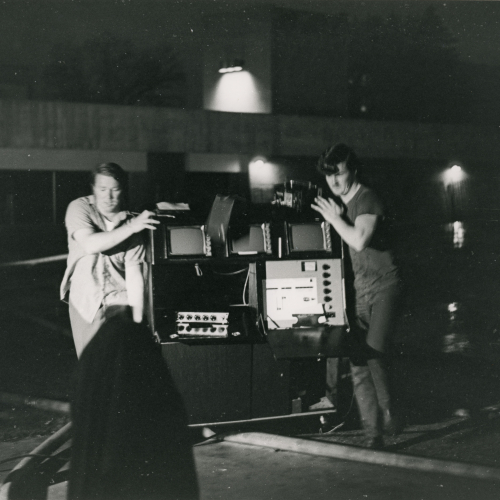 Two people rolling a cart filled with audio visual equipment outside