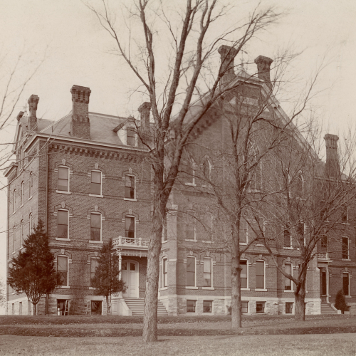 Three and a half story brick building with six visible chimneys and pointed arched window on the upper floor