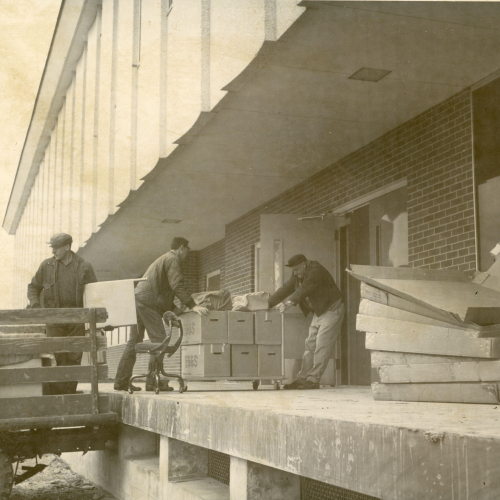 Three men unloading carts of boxes from back of a truck