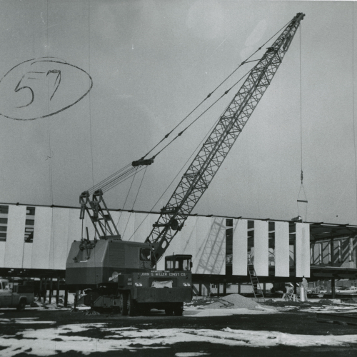 Crane adding material to partially-completed building, sides are almost paneled in