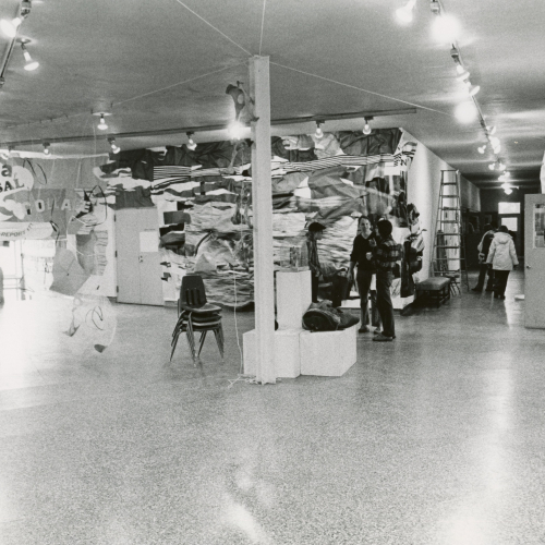 Art gallery exhibit with large pieces covering walls, about five people wandering through the gallery