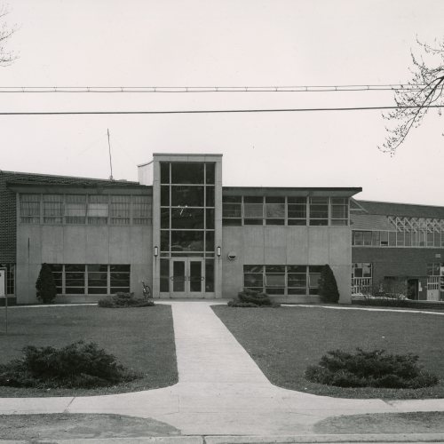 Entrance to a brick and limestone building with many windows; sign at front reads: Arts & Industries Building, Art Department, Exhibit Gallery, Industrial Arts Department
