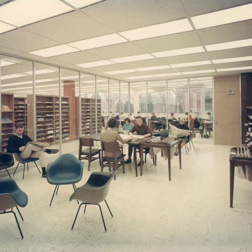 Students reading newspapers at tables and chairs in glassed-in room