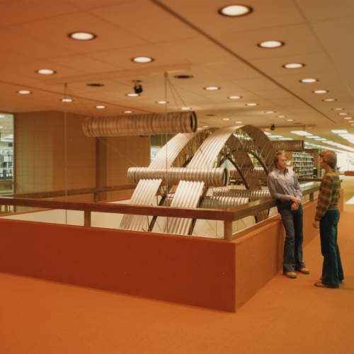 Two students talking next to a sculpture made of corrugated steel