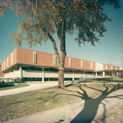 Red brick and tan stone building with autumn trees in front of it