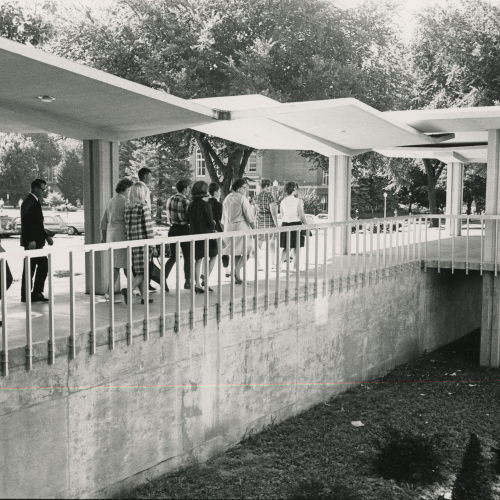 People walking under covered sidewalk toward entrance of building to the right