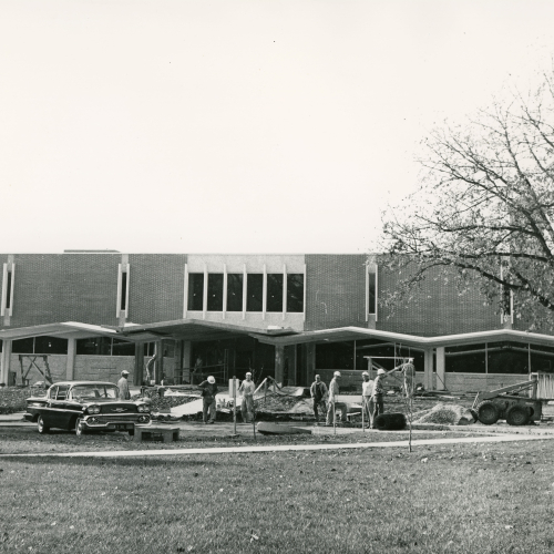 Construction workers on lawn/sidewalk in front of completed building
