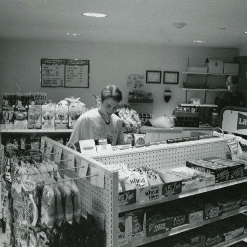 One student shopping in convenience store and another checking out at register