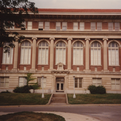 Front of a red brick and limestone building that has arched windows and pillars