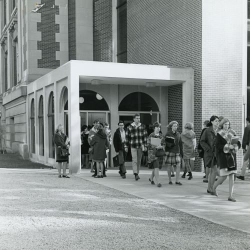 People exiting a brick and limestone building, sign to left reads: Seerley Hall business and business education