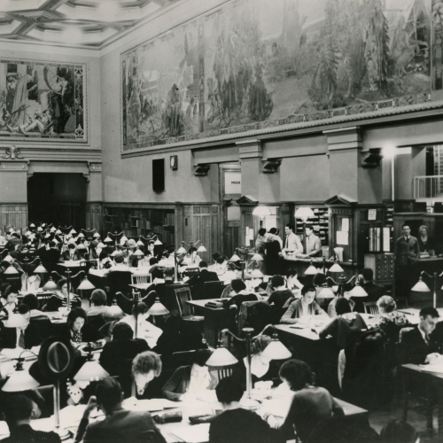 Large room filled with students studying at tables, murals on the upper parts of the surrounding walls