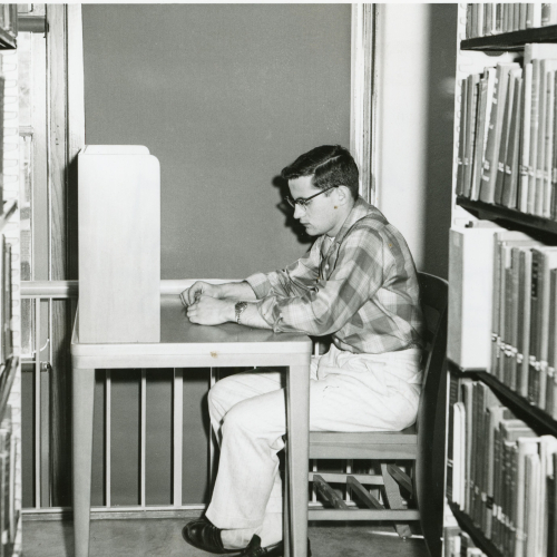 Man studying at carrel desk set in between two library stacks
