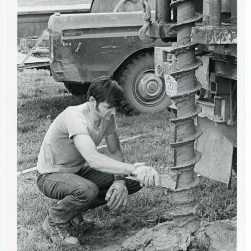 Man scraping soil off a large drill