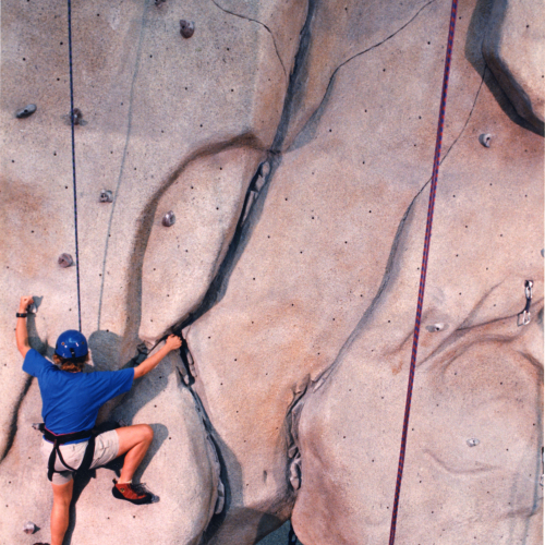 Person climbing a rock wall with a harness and helmet
