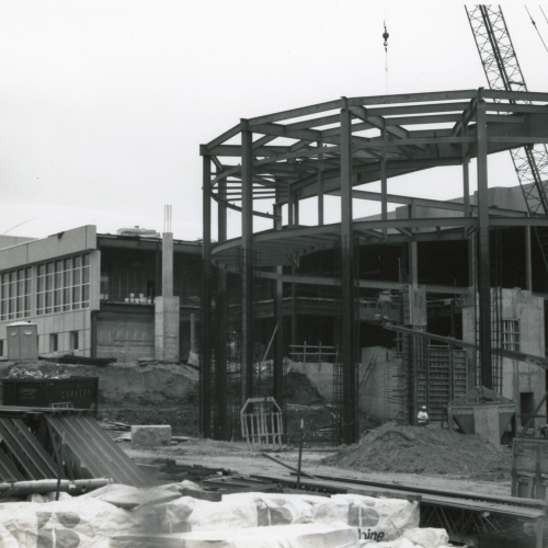 Crane placing beams onto partially-completed structure with a curved front