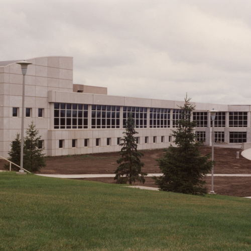 Across a green lawn, a limestone building with many large windows and a curved-facade entrance at the far right