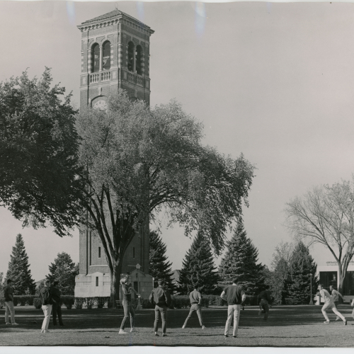 About 11 men tossing a football beside the Campanile