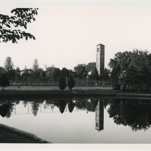 Campanile across tennis courts, reflected in pond in the foreground