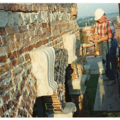 Mason on scaffolding assessing bricks near top of Campanile