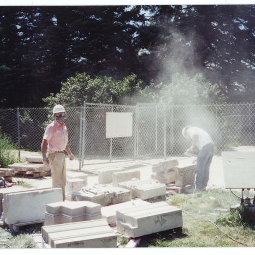Masons cleaning limestone trim on ground, dust in air
