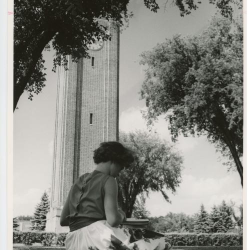 Woman sitting in grass with study materials, Campanile in background