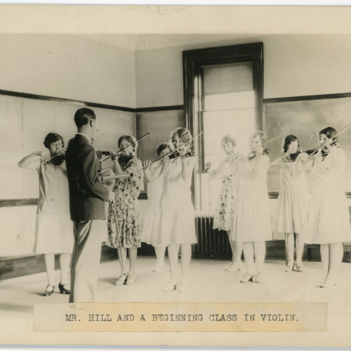 Eight students playing violin and one director, caption reads: Mr. Hill and a beginning class in violin