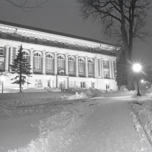 Brick and limestone building with arched windows and pillars on front lit up on a snowy night
