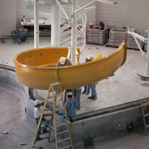 5 workers in hard hats installing the bottom loop of a yellow waterslide