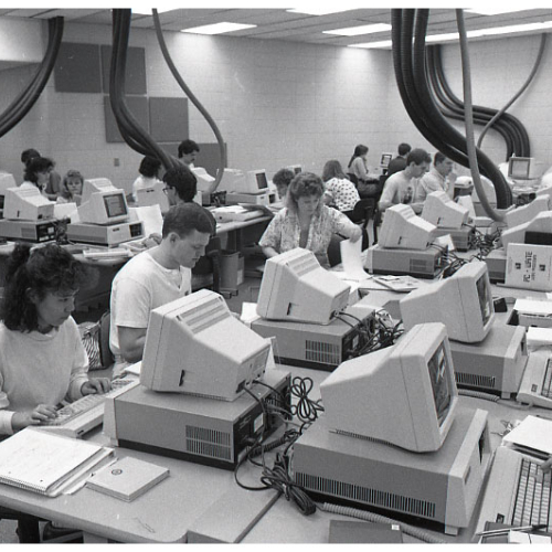 Many students working at stations in computer lab, large, thick cables descending from ceiling