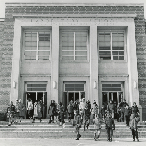 Crowd of children and adults leaving building with three double-door entrance and going down stairs; engraving over lintel reads "Laboratory School Iowa State Teachers College"