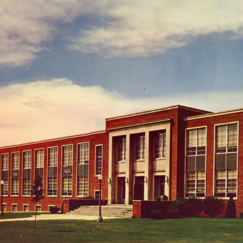 Colorized postcard of a two-story red brick building with high windows and limestone accents