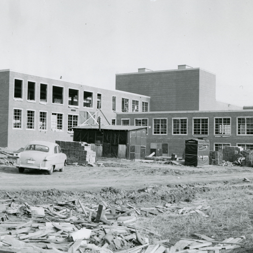 Construction in progress on a brick building with three wings of various heights, windows going into left section; car and scattered materials in front