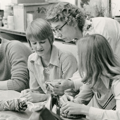 Woman teaching four students or student teachers about a yarn project in a classroom