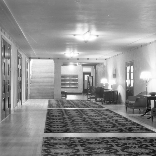 Hallway with carpet down the center, four sets of closed double-doors to left, and couches and lighting to right